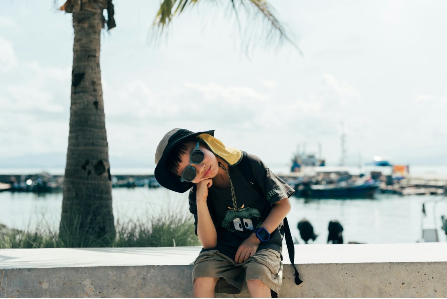 A child sits in sunglasses by a palm