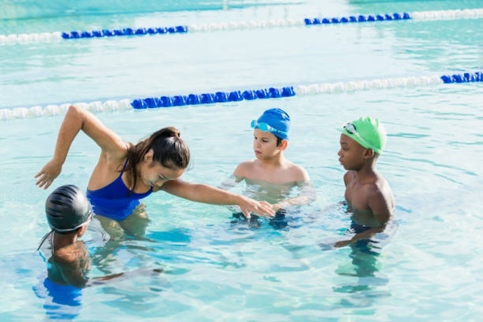  (alt-tag: Young female coach teaching children freestyle swimming in a pool)