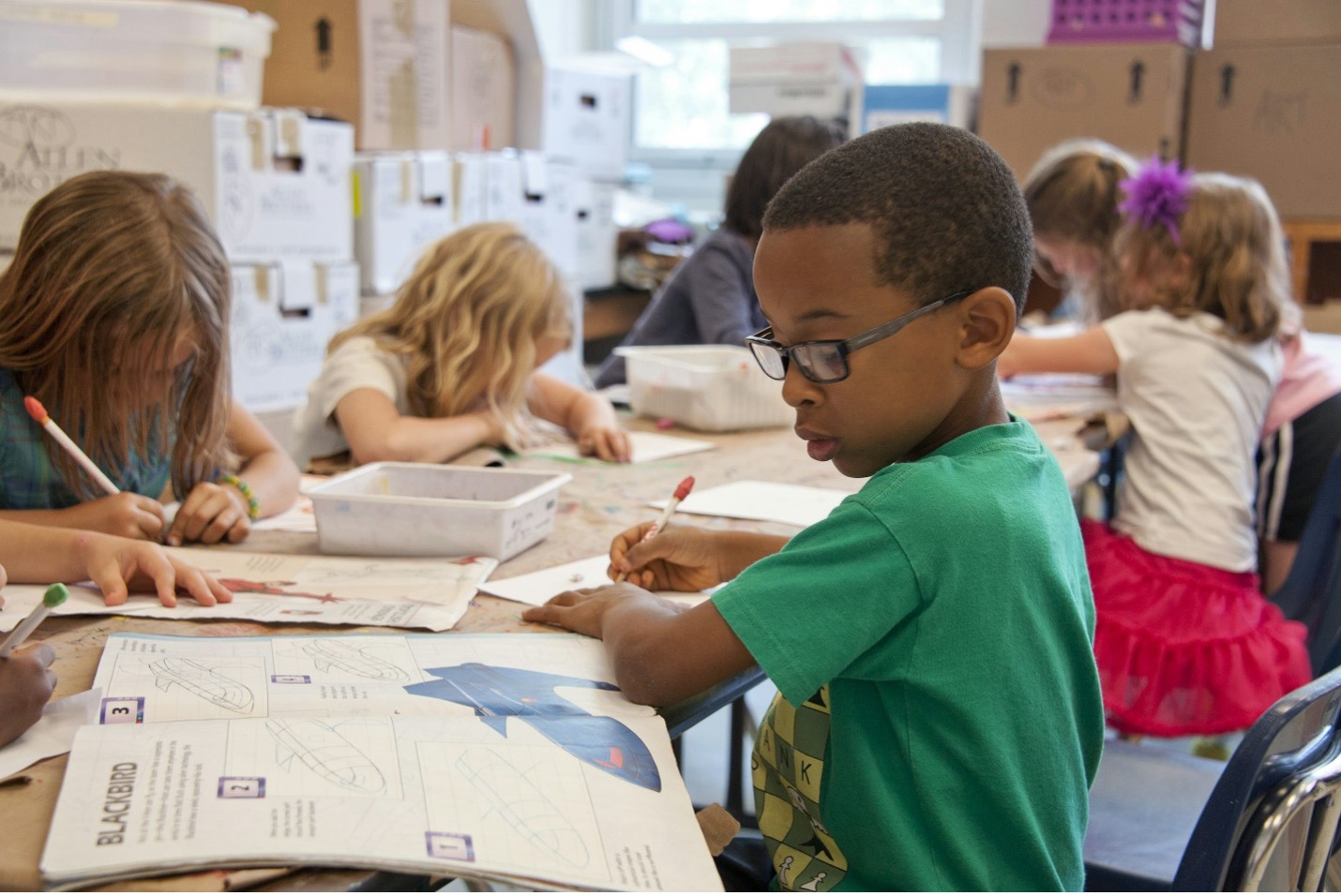 boy in green sweater writing on white paper